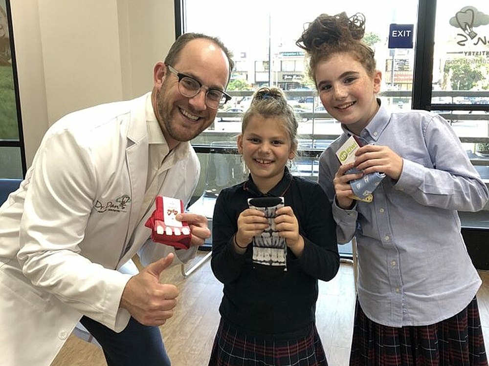 Smiling children with orthodontist and dental gifts.