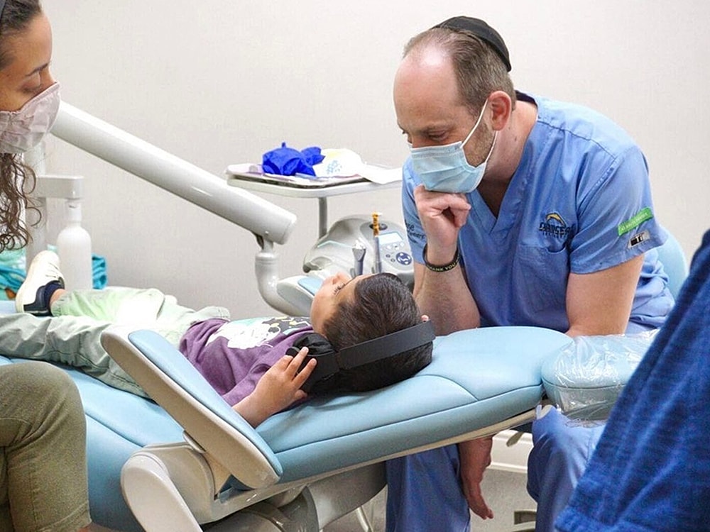 Child in dental chair with doctor and parent.