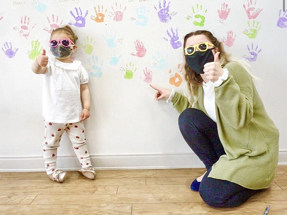 Child and adult giving thumbs up in front of handprints.
