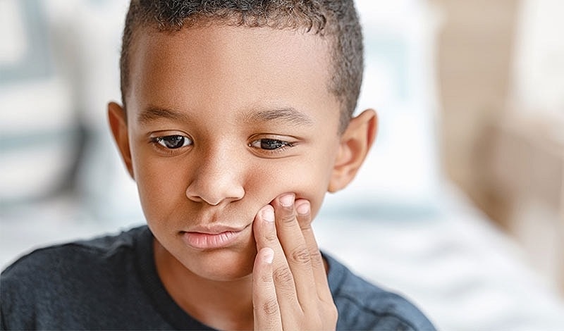 Boy touching his cheek, looking concerned.